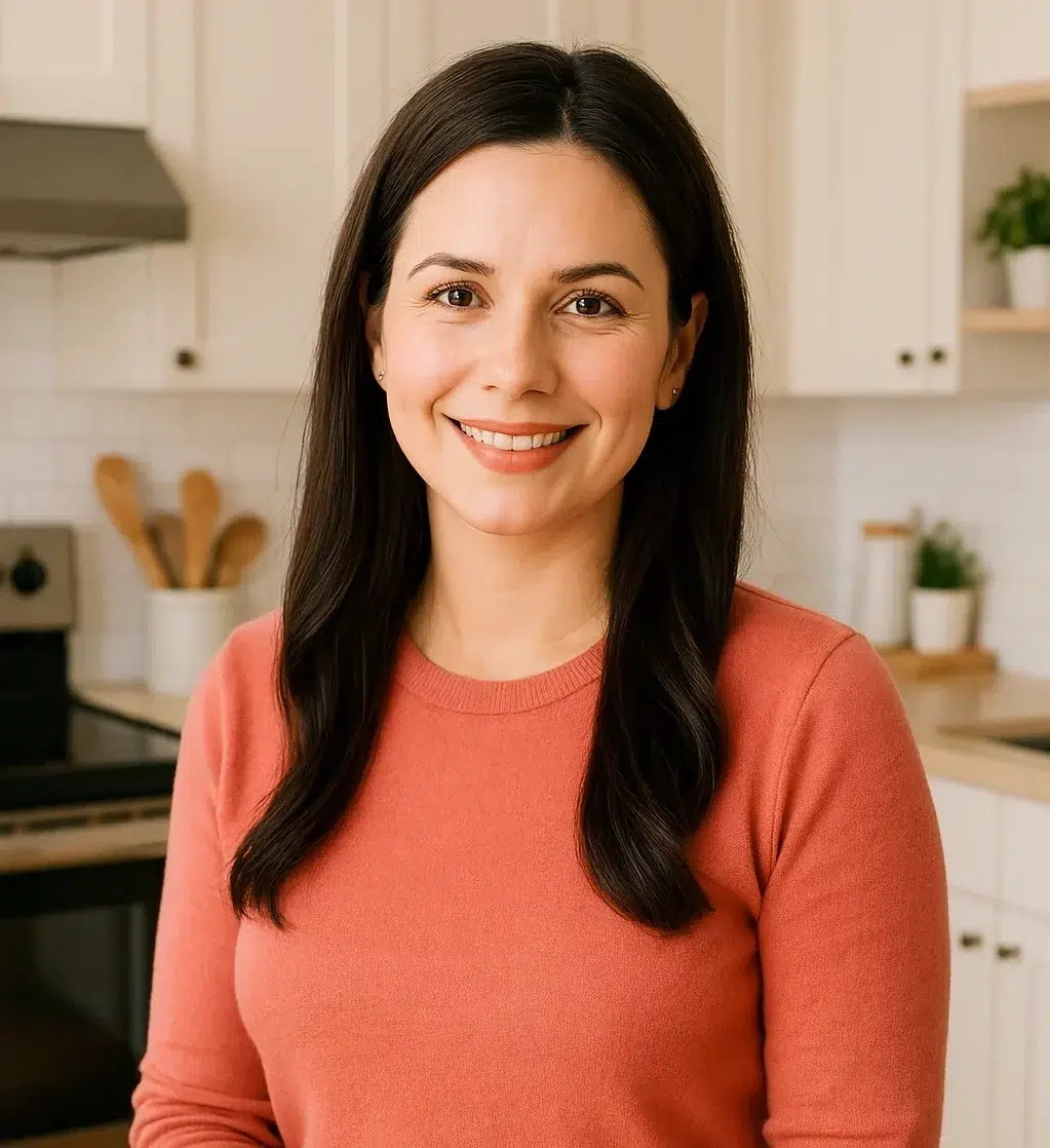 Smiling woman in a coral sweater standing in a bright, modern kitchen